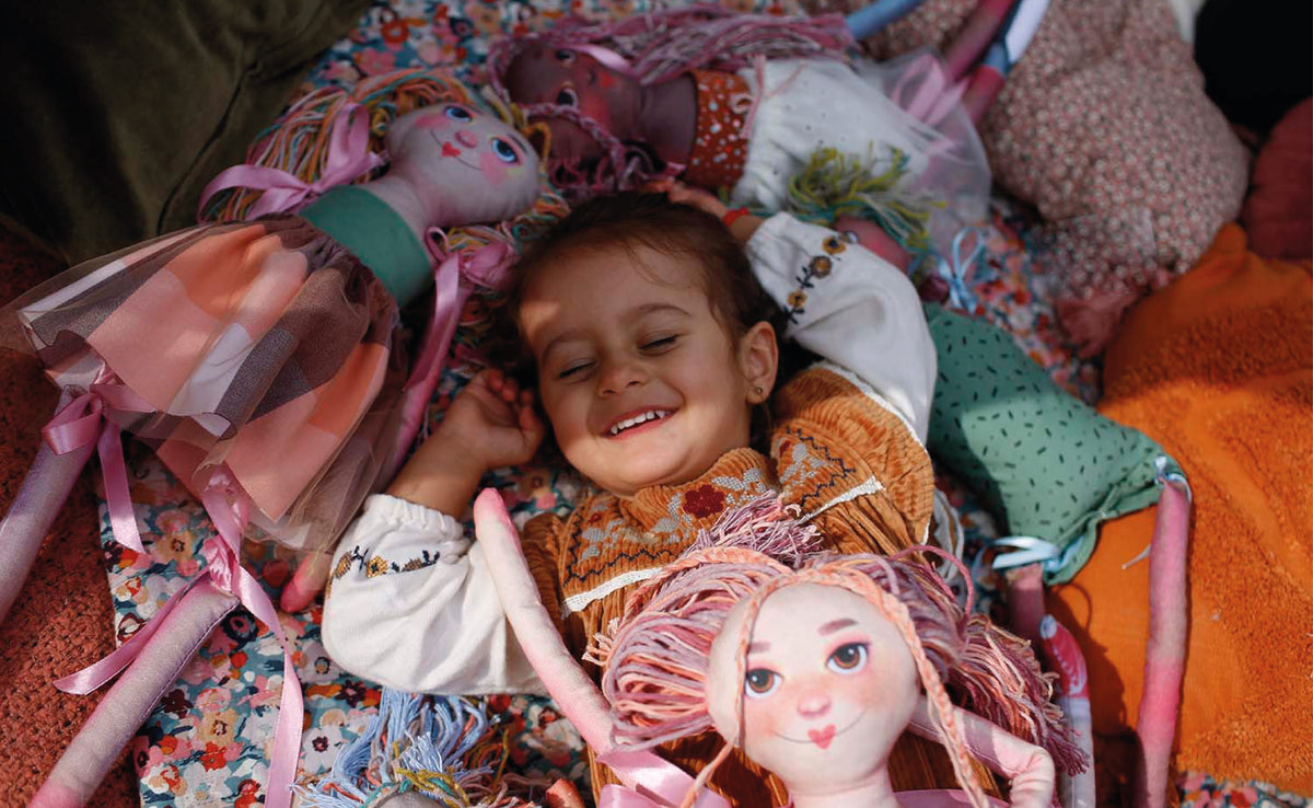 Dziewczynka leżąca z uśmiechem wśród lalek Kakala